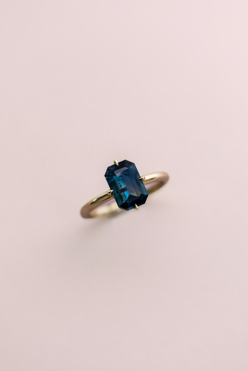 Gold ring with a blue gemstone on a light pink background