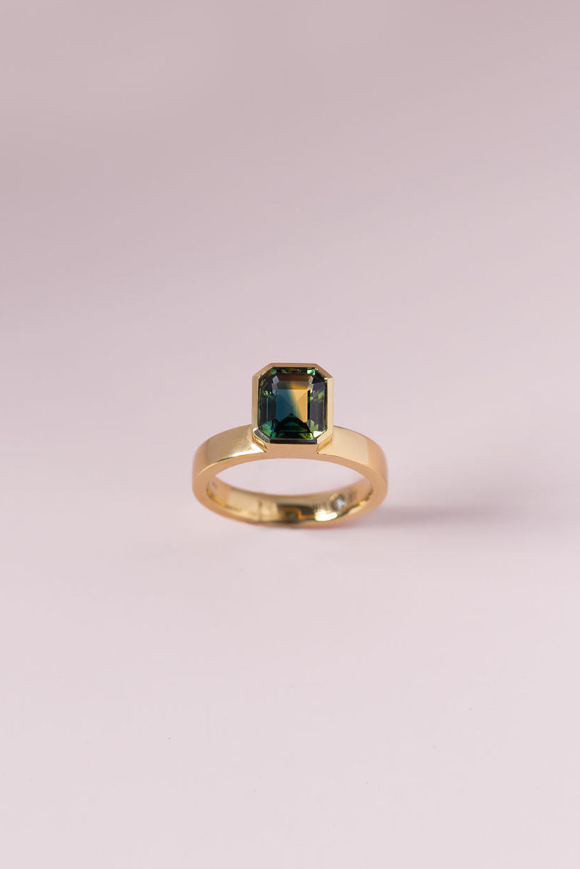 Gold ring with a green gemstone on a light pink background