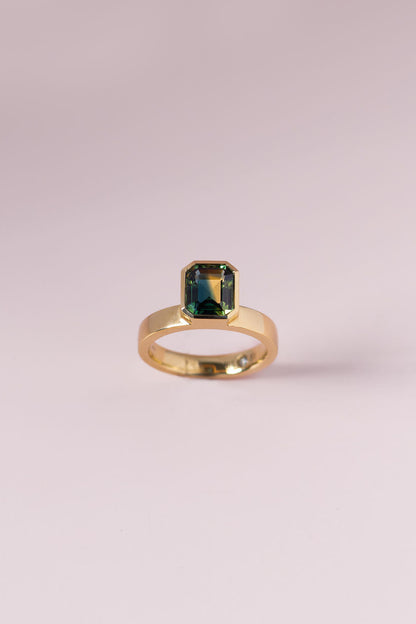 Gold ring with a green gemstone on a light pink background