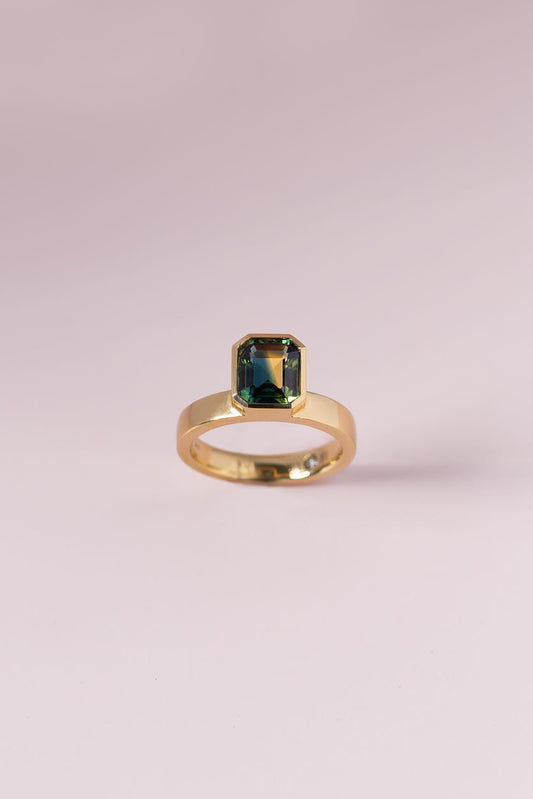 Gold ring with a green gemstone on a light pink background